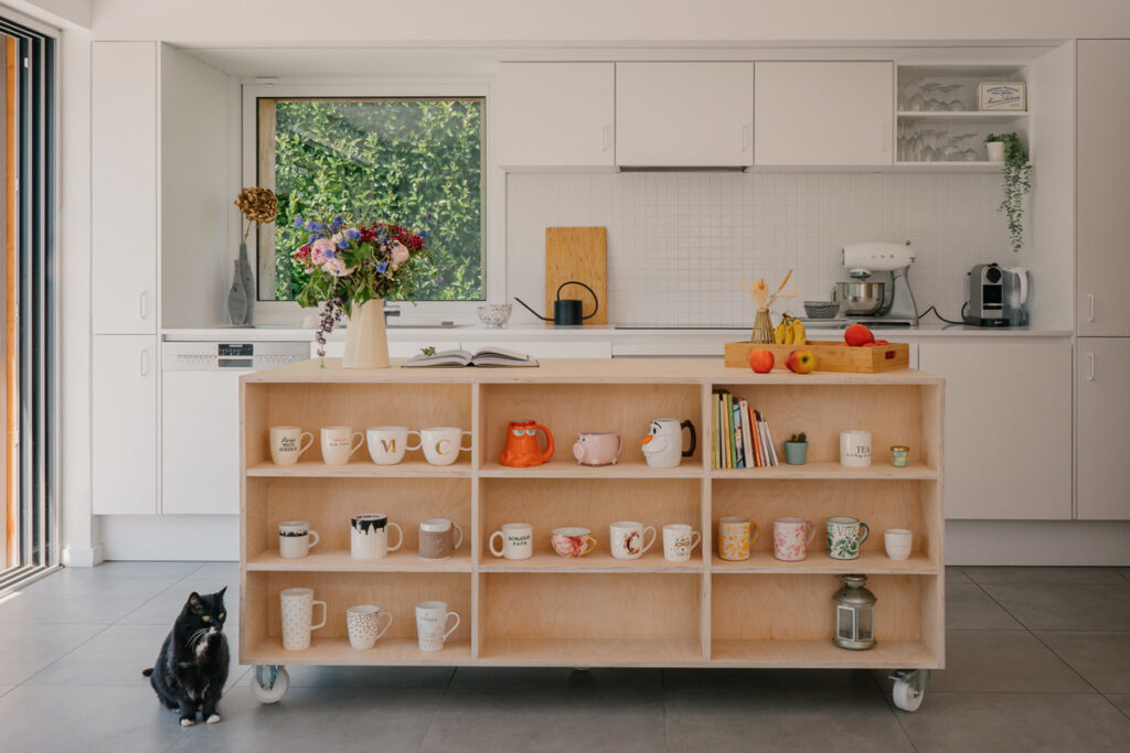 cuisine évolutive : le plan de travail en bois est pensé avec des roulettes pour pouvoir être déplacé facilement et la cuisine blanche est un espace neutre de la maison.